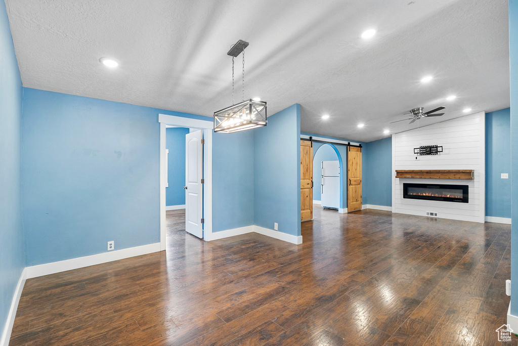 Unfurnished living room featuring a barn door, a ceiling fan, wood finished floors, recessed lighting, and a fireplace