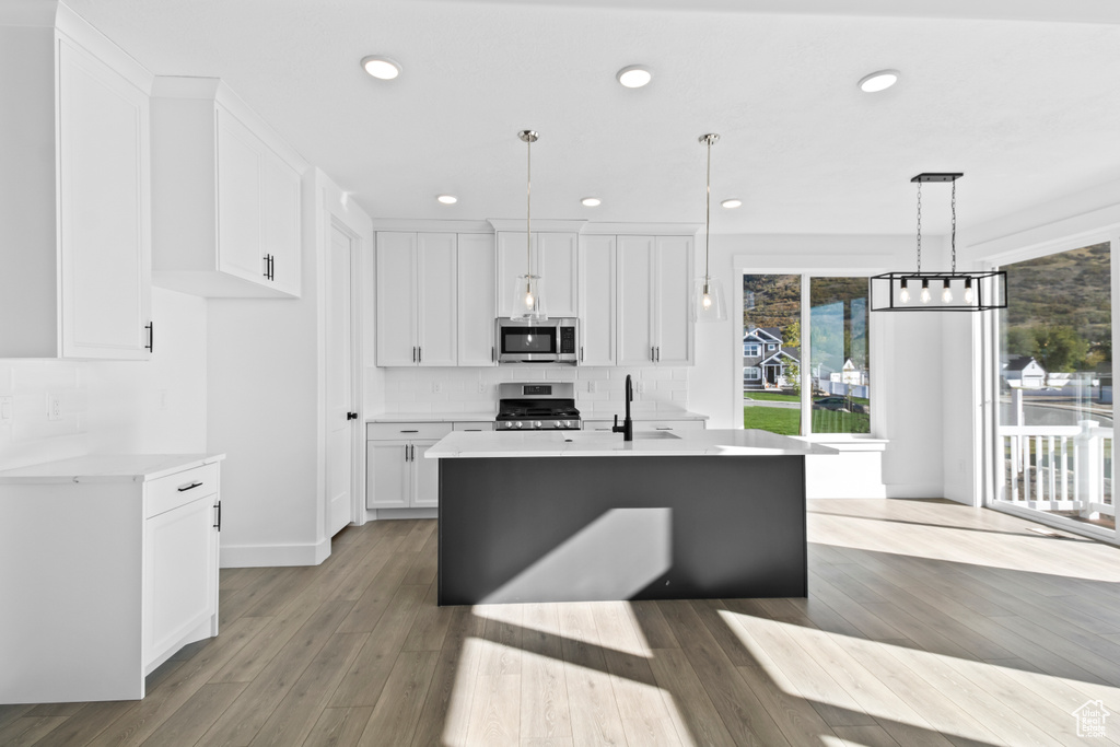 Kitchen featuring appliances with stainless steel finishes, light countertops, white cabinets, decorative backsplash, and wood finished floors
