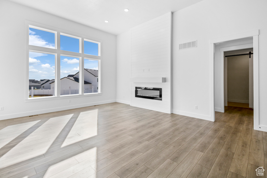 Unfurnished living room featuring light wood-style floors, a glass covered fireplace, a barn door, and recessed lighting