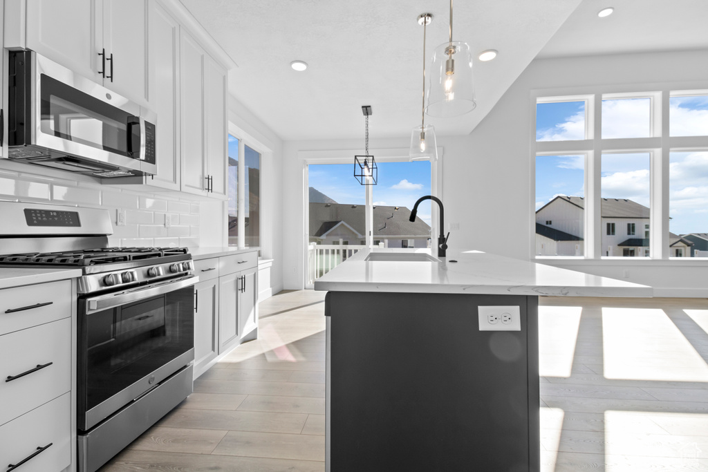 Kitchen with appliances with stainless steel finishes, recessed lighting, a kitchen island with sink, backsplash, and light wood finished floors