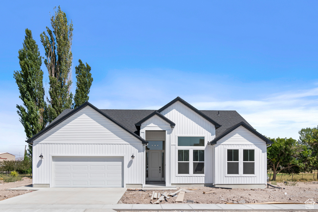 Modern inspired farmhouse with an attached garage, driveway, a shingled roof, and board and batten siding