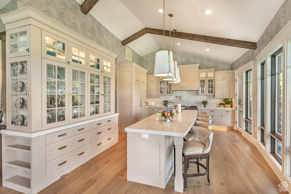 Kitchen featuring beam ceiling, light countertops, light wood-style floors, an island with sink, and open shelves