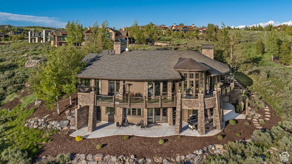 Back of property with a chimney, a patio area, stone siding, and a wooden deck