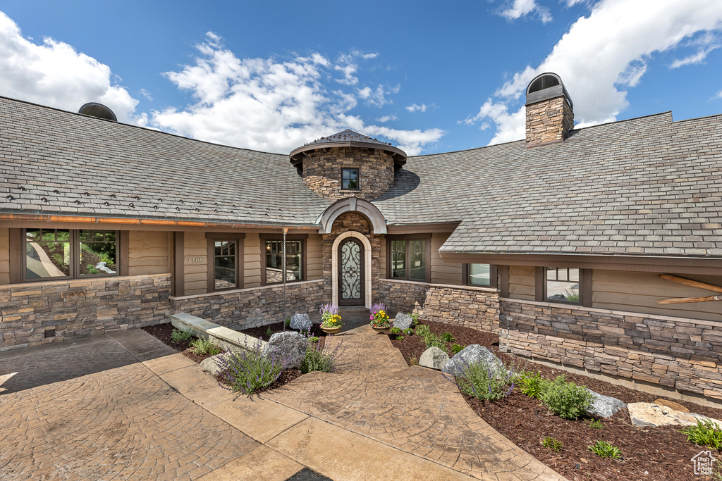 Doorway to property featuring stone siding, a high end roof, and a chimney
