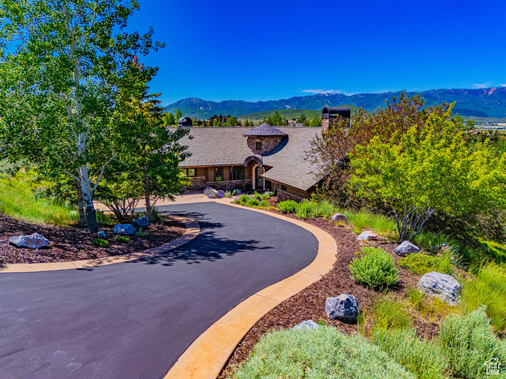 View of front of home featuring a mountain view, stone siding, curved driveway, and a chimney