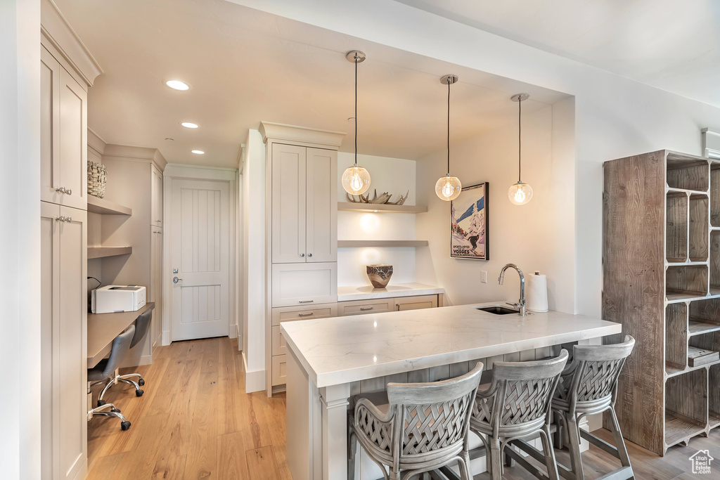 Kitchen with open shelves, a peninsula, a breakfast bar, light wood-style flooring, and pendant lighting