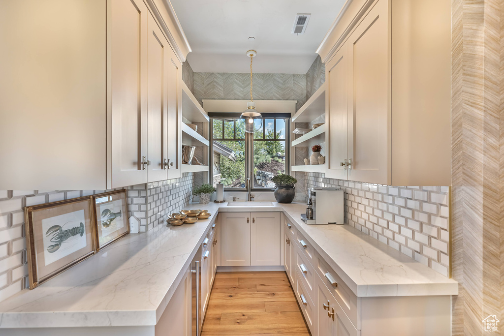 Kitchen with open shelves, light stone counters, decorative backsplash, light wood-style flooring, and pendant lighting