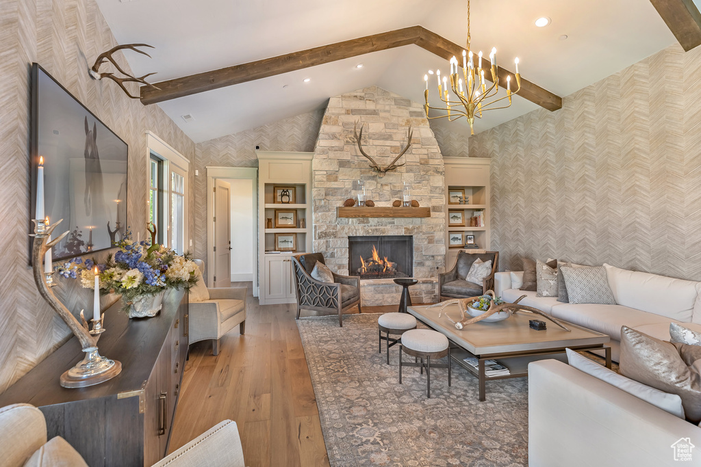 Living room featuring wallpapered walls, light wood finished floors, beamed ceiling, a chandelier, and a fireplace