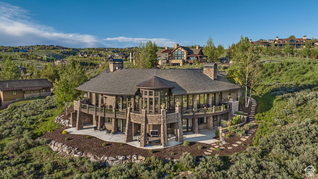 Back of property with a patio area, a chimney, stone siding, and a deck