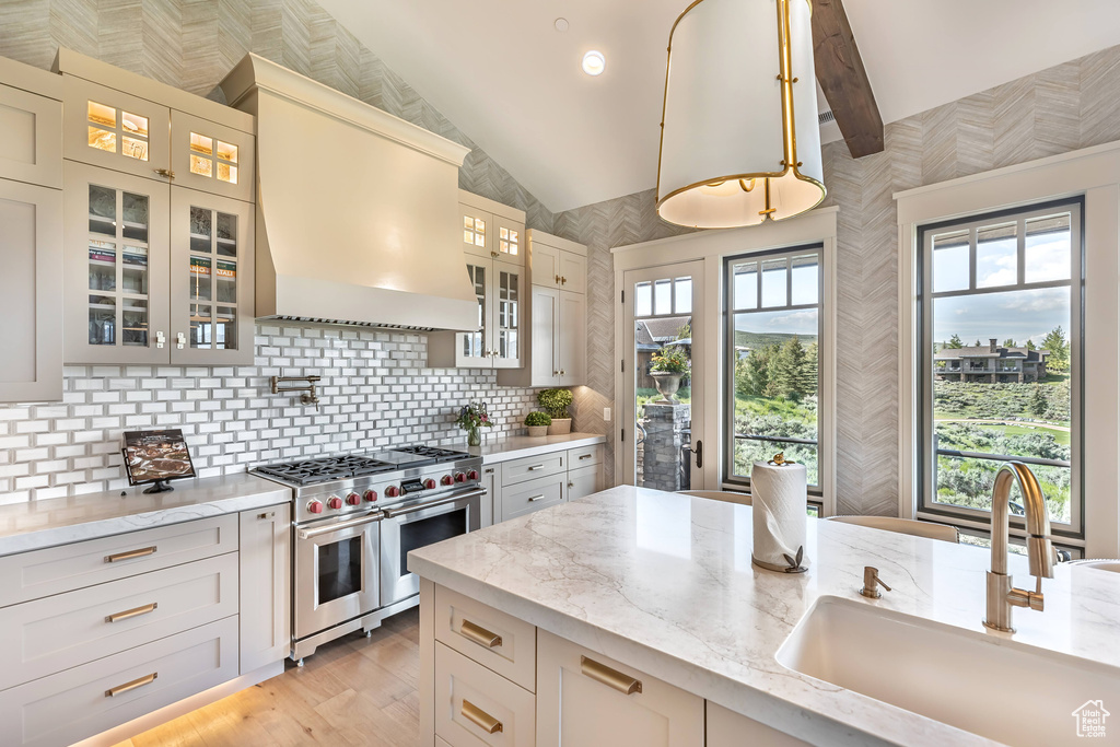 Kitchen with range with two ovens, custom range hood, light stone counters, tasteful backsplash, and vaulted ceiling