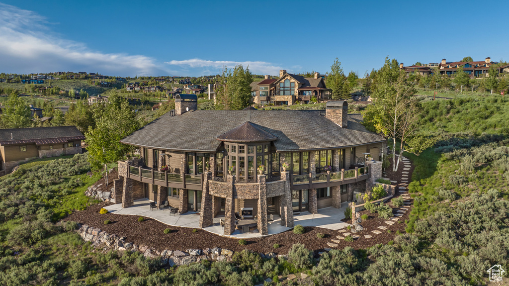 Rear view of house featuring a patio area, a chimney, and stone siding