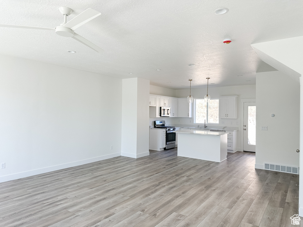 Kitchen featuring stainless steel appliances, light wood-type flooring, a kitchen island, white cabinetry, and light countertops