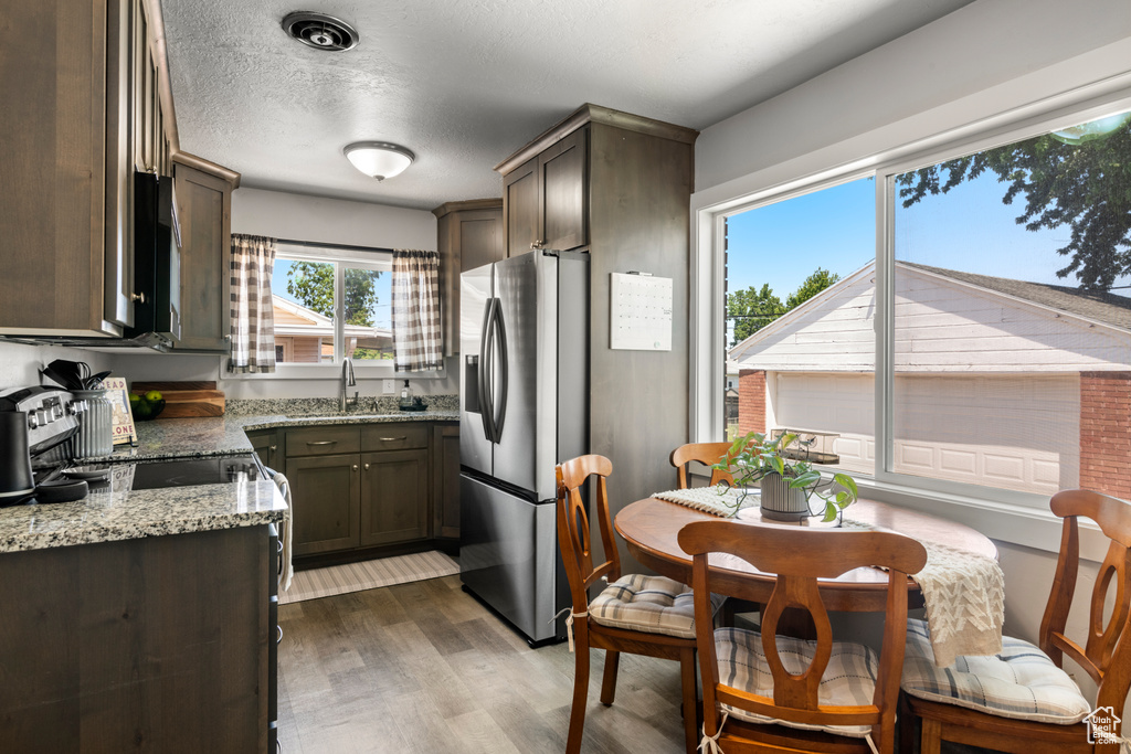 Kitchen featuring stainless steel fridge with ice dispenser, wood finished floors, light stone counters, dark brown cabinetry, and a textured ceiling