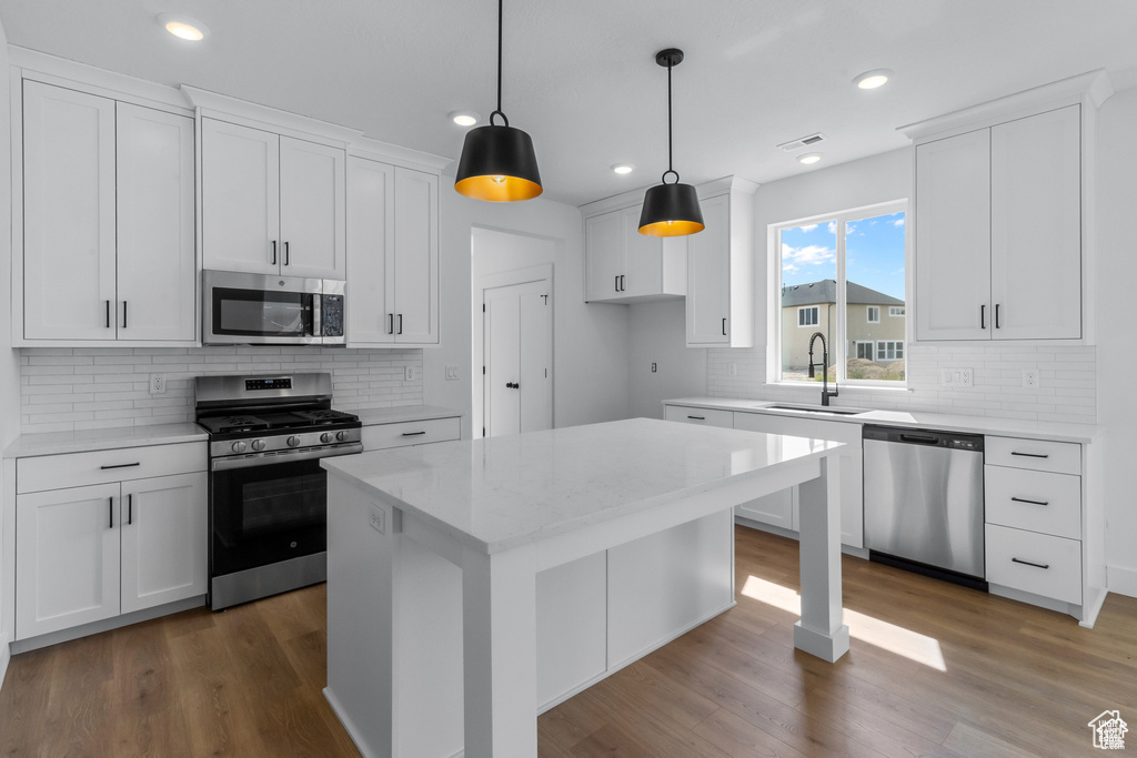 Kitchen featuring appliances with stainless steel finishes, decorative backsplash, white cabinets, wood finished floors, and recessed lighting