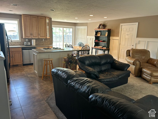 Living area with a textured ceiling, wainscoting, recessed lighting, dark tile patterned floors, and a decorative wall