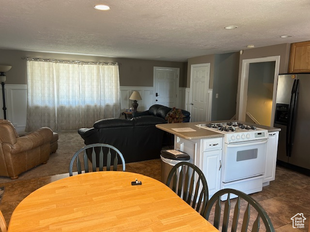 Kitchen featuring white gas range oven, stainless steel fridge with ice dispenser, open floor plan, a textured ceiling, and a center island