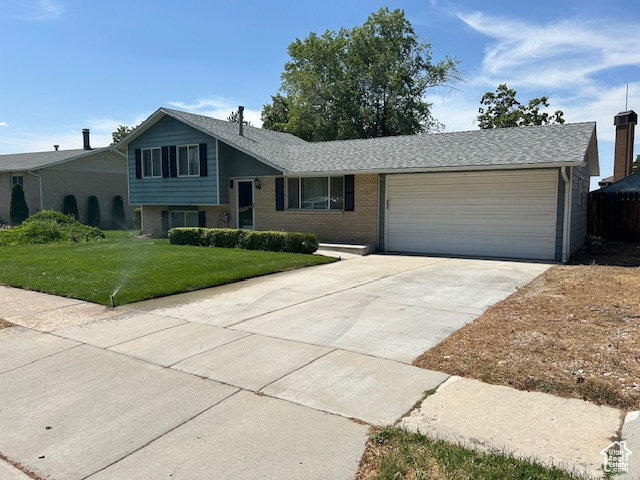 Split level home featuring a garage, concrete driveway, a front yard, and brick siding