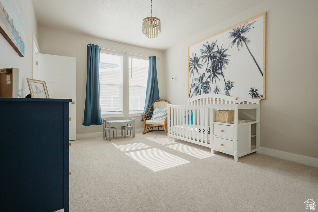 Carpeted bedroom featuring a chandelier and a nursery area