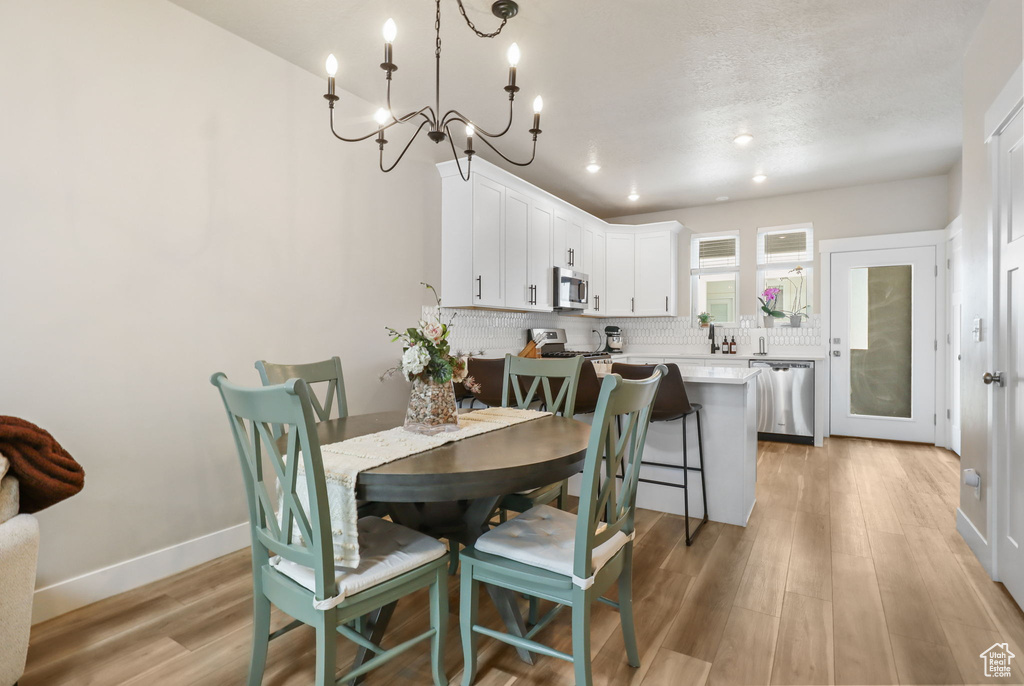 Dining room featuring light wood-style floors, a chandelier, recessed lighting, and a textured ceiling