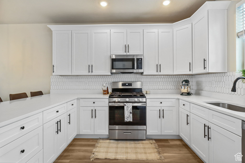 Kitchen featuring stainless steel appliances, white cabinetry, light countertops, recessed lighting, and decorative backsplash