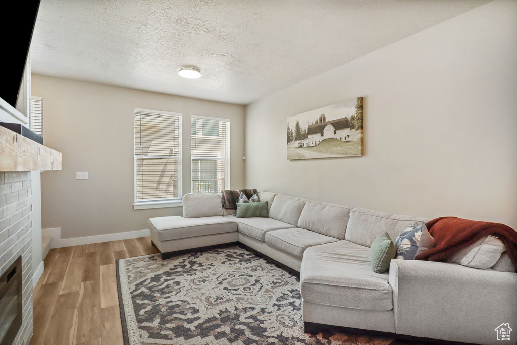 Living area with a brick fireplace, wood finished floors, and a textured ceiling
