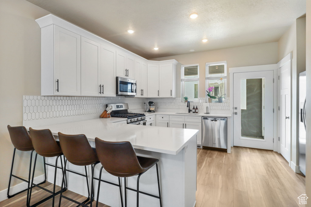 Kitchen with stainless steel appliances, a peninsula, light countertops, white cabinetry, and a breakfast bar