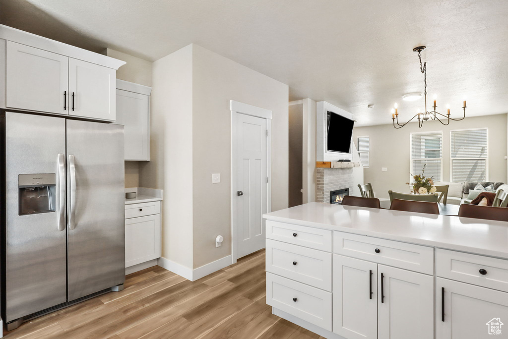 Kitchen with stainless steel refrigerator with ice dispenser, open floor plan, a chandelier, light wood-style flooring, and white cabinets