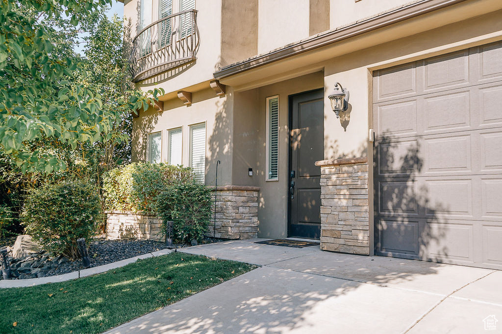 Entrance to property featuring a garage, stucco siding, stone siding, and a balcony