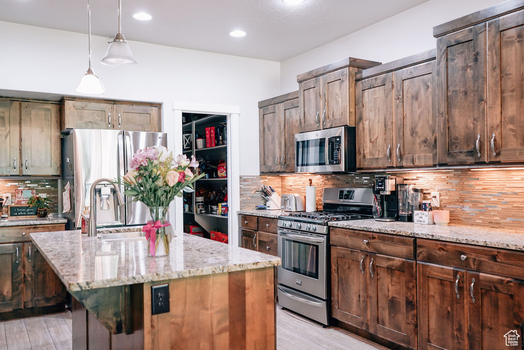 Kitchen featuring stainless steel appliances, light stone countertops, light wood-style floors, tasteful backsplash, and a kitchen island