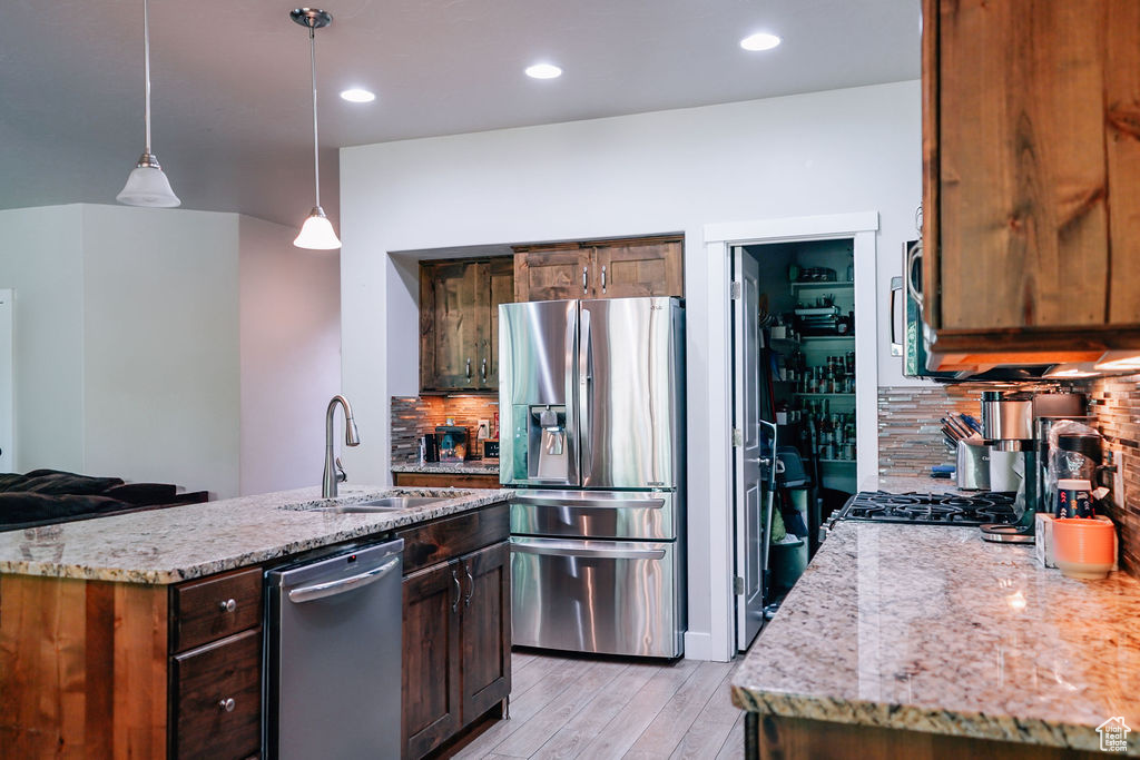 Kitchen featuring stainless steel appliances, decorative backsplash, light wood finished floors, light stone counters, and pendant lighting