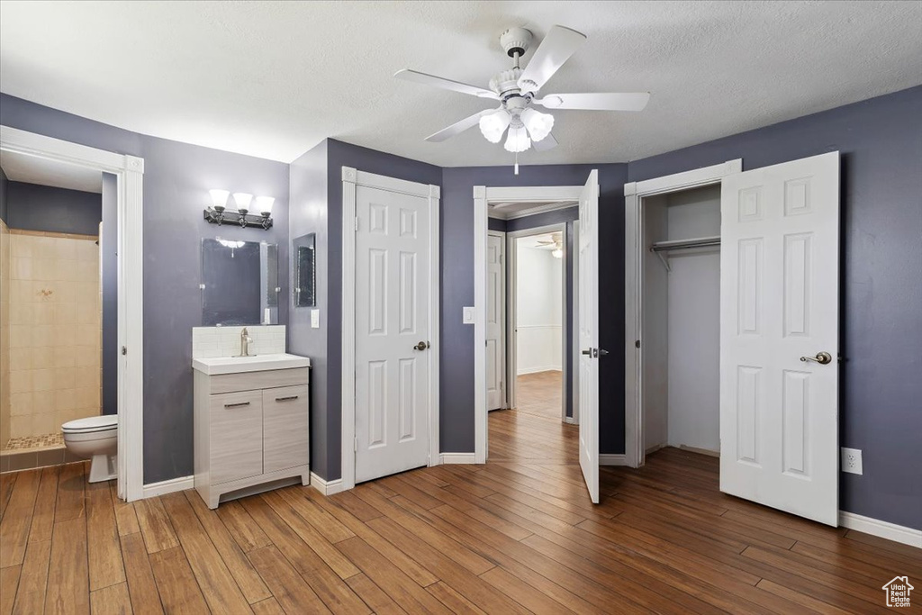Unfurnished bedroom featuring wood finished floors, connected bathroom, multiple closets, a ceiling fan, and a textured ceiling