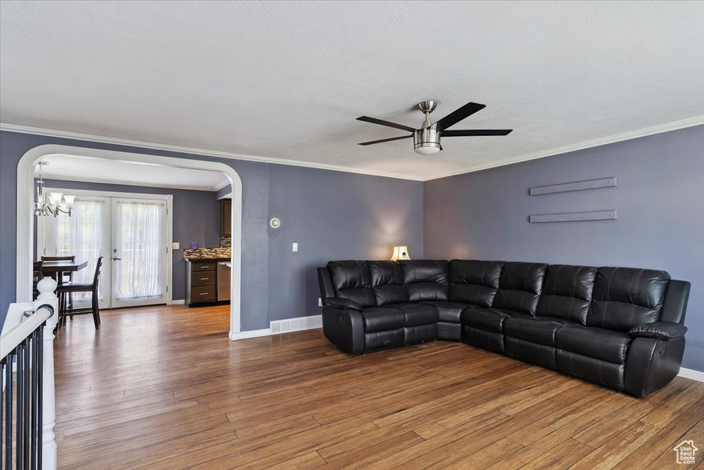 Living area featuring arched walkways, ceiling fan, wood finished floors, ornamental molding, and a chandelier