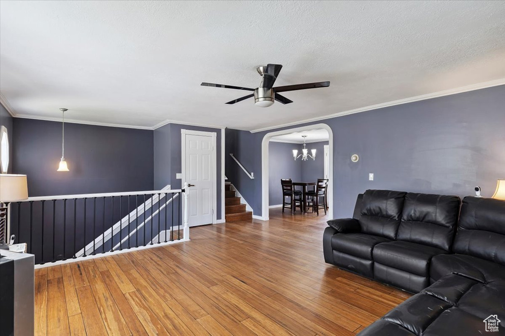 Living area featuring arched walkways, a chandelier, wood finished floors, ceiling fan, and ornamental molding