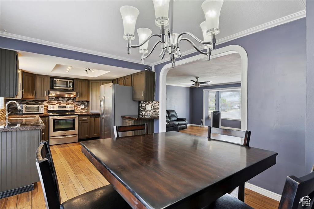 Dining space featuring arched walkways, crown molding, a chandelier, light wood finished floors, and ceiling fan
