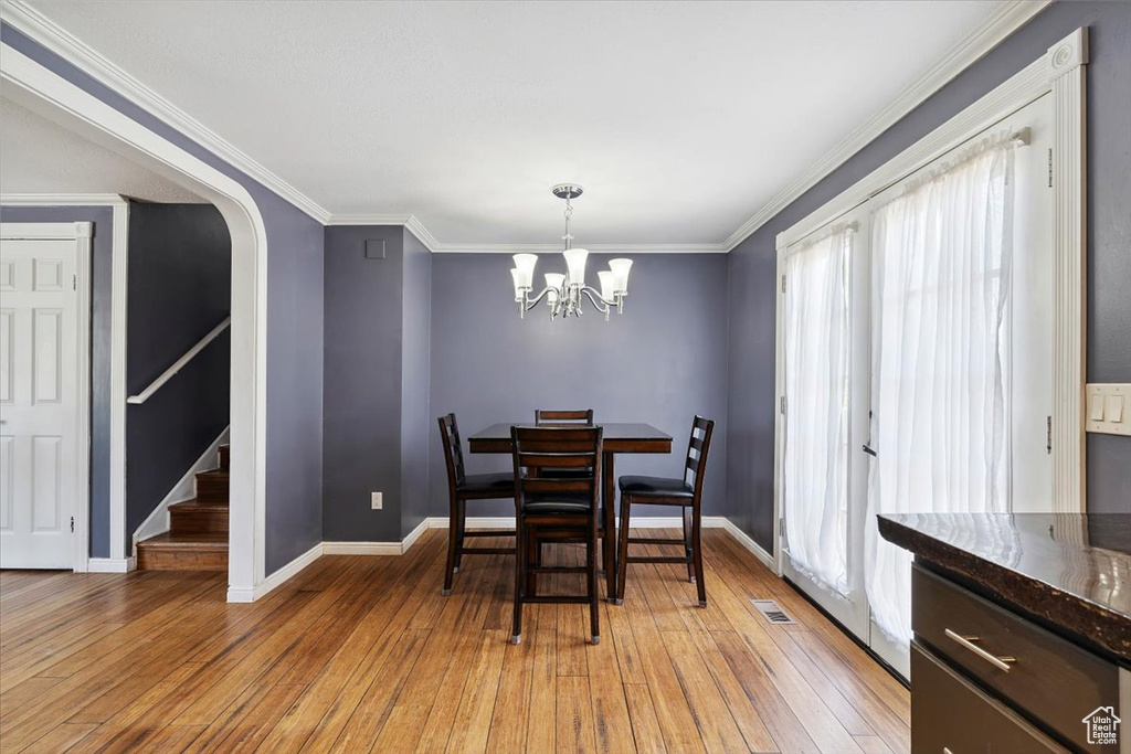 Dining room with light wood-style flooring, stairway, crown molding, a chandelier, and arched walkways