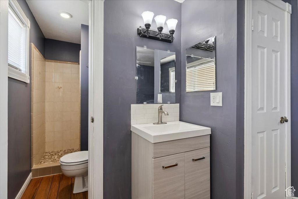 Full bath with vanity, tiled shower, wood finished floors, and decorative backsplash