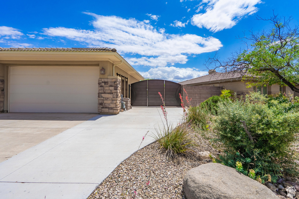 View of side of home featuring concrete driveway, stone siding, a gate, a tile roof, and a garage