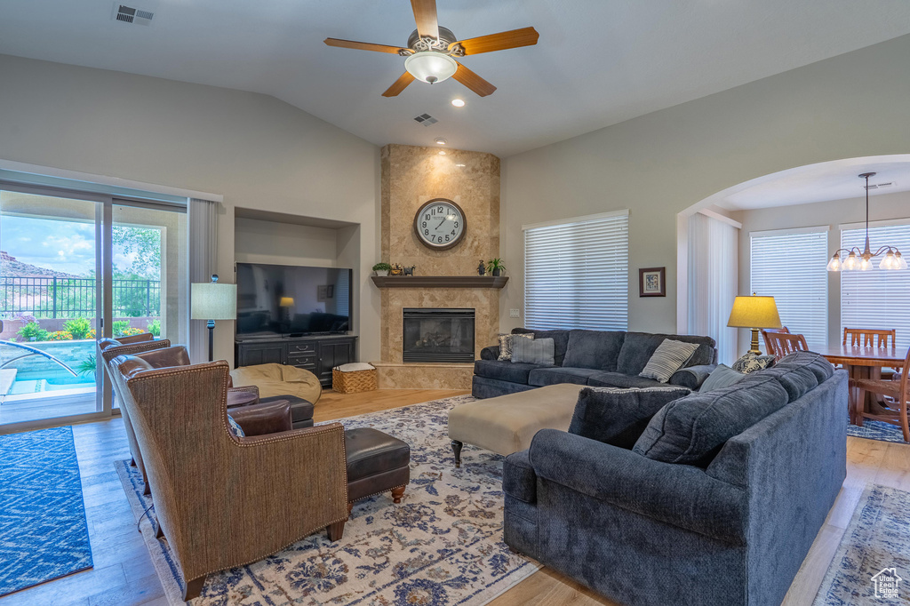 Living area with light wood finished floors, arched walkways, a chandelier, a ceiling fan, and vaulted ceiling