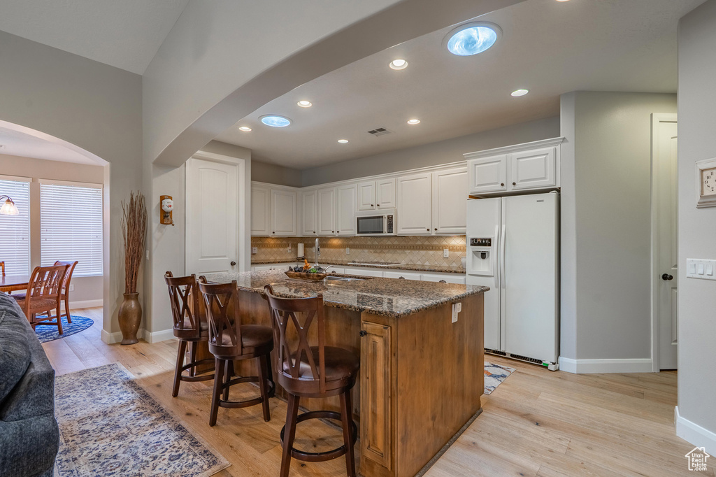 Kitchen with white appliances, arched walkways, light wood-type flooring, dark stone counters, and a center island