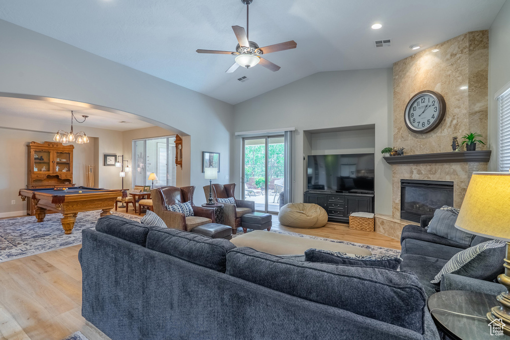 Living room featuring wood finished floors, pool table, a fireplace, arched walkways, and vaulted ceiling