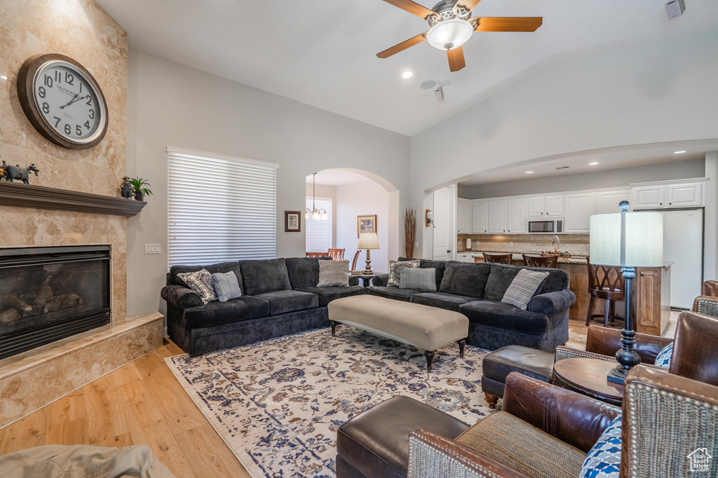 Living room featuring arched walkways, lofted ceiling, light wood-type flooring, ceiling fan, and a premium fireplace