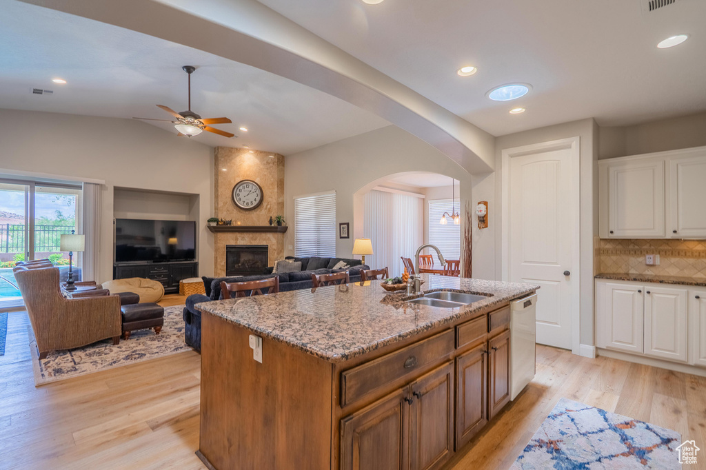 Kitchen featuring white dishwasher, arched walkways, light stone counters, decorative backsplash, and white cabinets