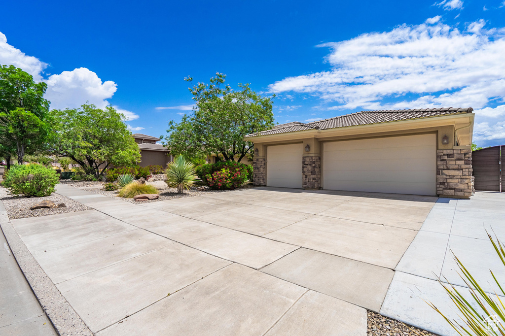 View of front of property featuring stone siding, driveway, an attached garage, and a tiled roof
