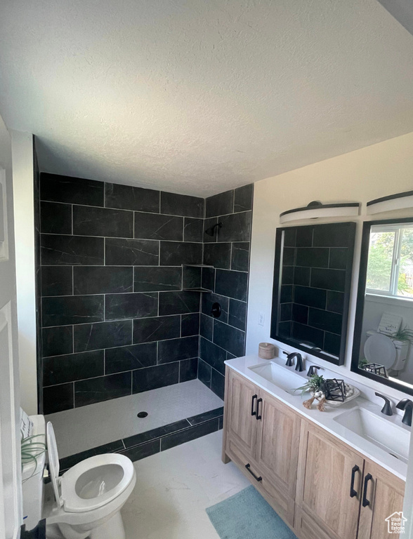 Bathroom with a tile shower, double vanity, and a textured ceiling