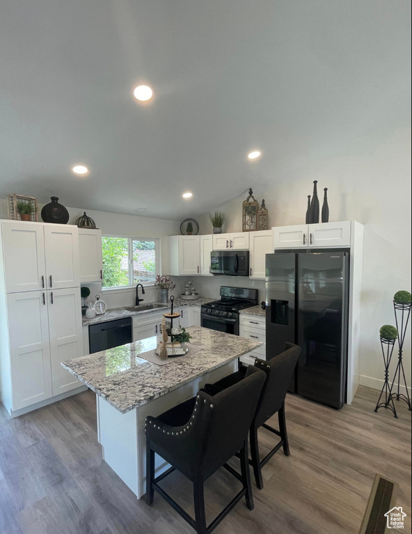 Kitchen with black appliances, a breakfast bar, white cabinets, a center island, and light stone counters