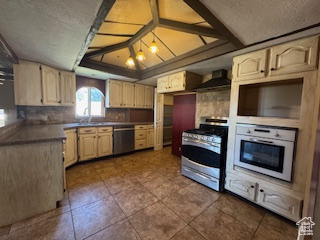 Kitchen with appliances with stainless steel finishes, wall chimney exhaust hood, dark tile patterned floors, light brown cabinets, and dark countertops