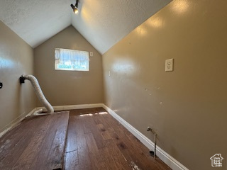 Empty room featuring hardwood / wood-style flooring, a textured ceiling, and vaulted ceiling