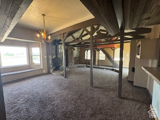 Below grade area featuring a chandelier, carpet flooring, a wood stove, and stairs