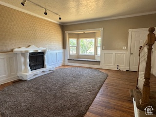 Unfurnished living room with a decorative wall, a fireplace with raised hearth, wood finished floors, wainscoting, and track lighting