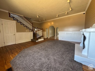 Unfurnished living room with crown molding, stairs, arched walkways, wood finished floors, and a decorative wall